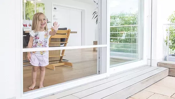 lachendes kleines Mädchen im Haus vor Schiebeanlage_Insektenschutz Firma Neuner GmbH lachendes kleines Mädchen im Haus vor Schiebeanlage_Insektenschutz Firma Neuner GmbH